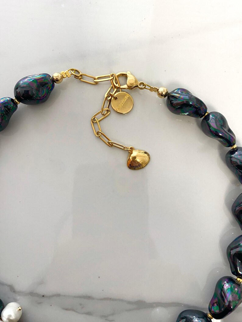 May include: A gold chain necklace with a black baroque pearl pendant. The chain has a lobster clasp and a small charm with the word "Madewell" on it.
