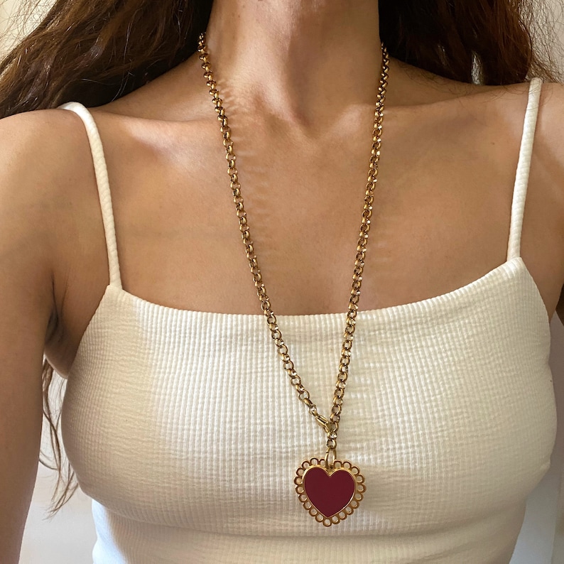 May include: A gold chain necklace with a large, red heart pendant. The heart has a decorative, scalloped edge.