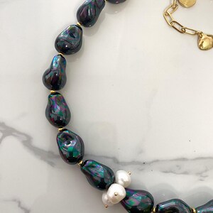 May include: A black and iridescent pearl necklace with a gold chain and a cluster of white pearls and green beads.