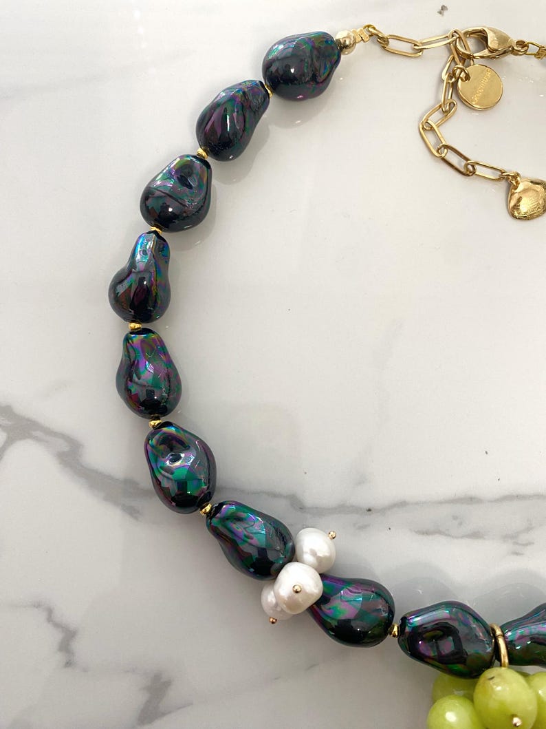 May include: A black and iridescent pearl necklace with a gold chain and a cluster of white pearls and green beads.