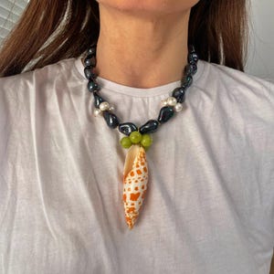 May include: A black and white pearl necklace with a green and orange seashell pendant.
