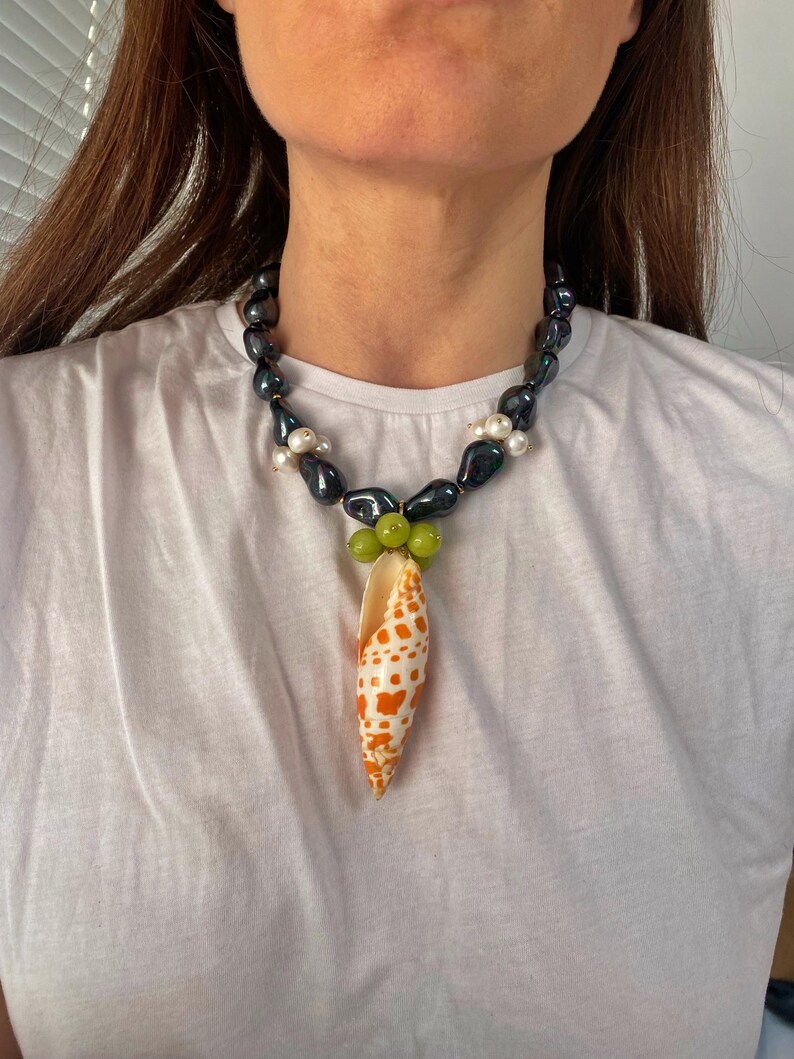 May include: A black and white pearl necklace with a green and orange seashell pendant.