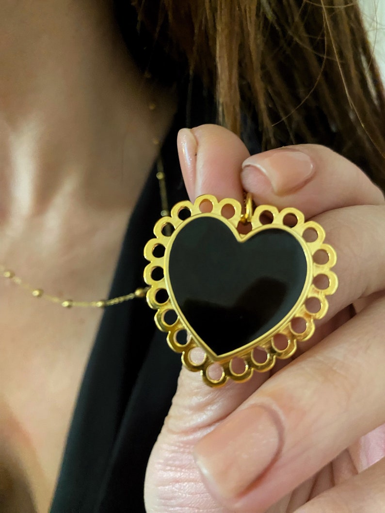 Pu&ograve; includere: Una collana con un ciondolo a forma di cuore in oro, con un centro in smalto nero e un bordo delicato a forma di conchiglia.
