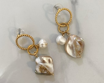 May include: A pair of gold earrings with a pearl and a large, irregularly shaped pearl drop. The earrings feature a small gold circle with a beaded edge.