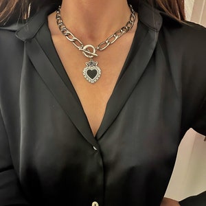May include: A silver chain necklace with a large, black heart pendant. The heart has a silver frame and a rose design at the top.