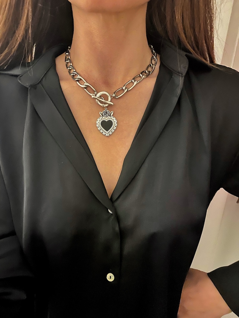 May include: A silver chain necklace with a large, black heart pendant. The heart has a silver frame and a rose design at the top.