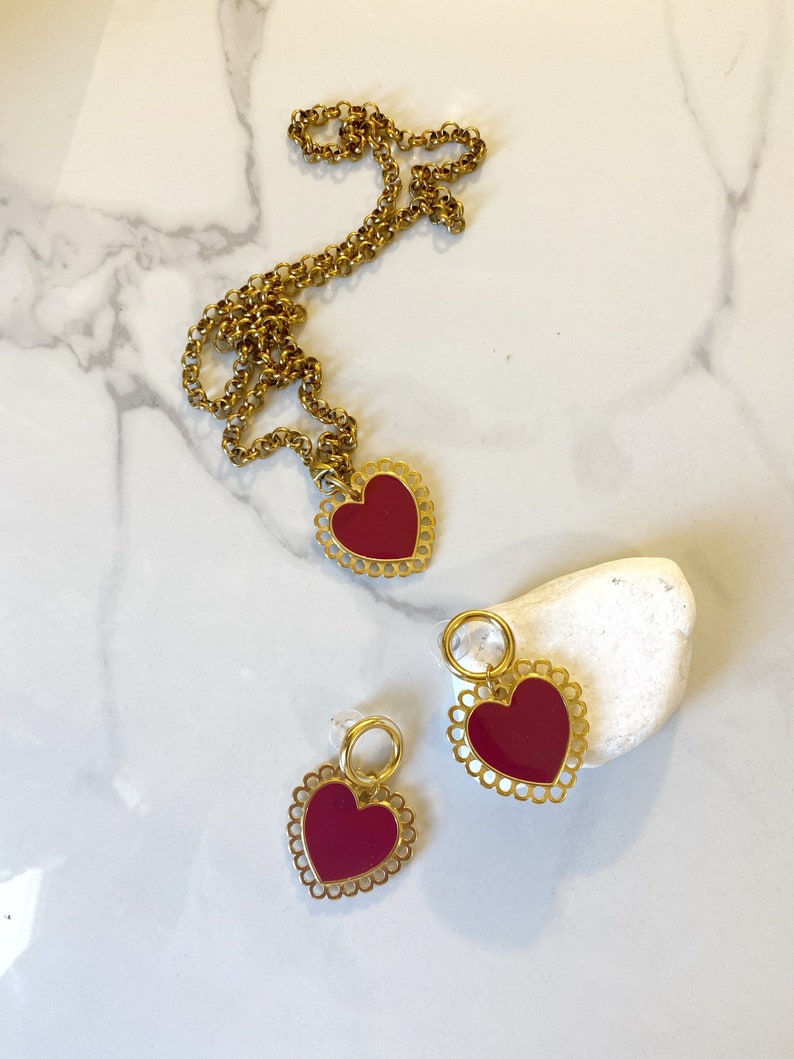 May include: A gold chain necklace with a red heart pendant and a pair of matching red heart earrings. The heart pendants have a delicate, scalloped edge.