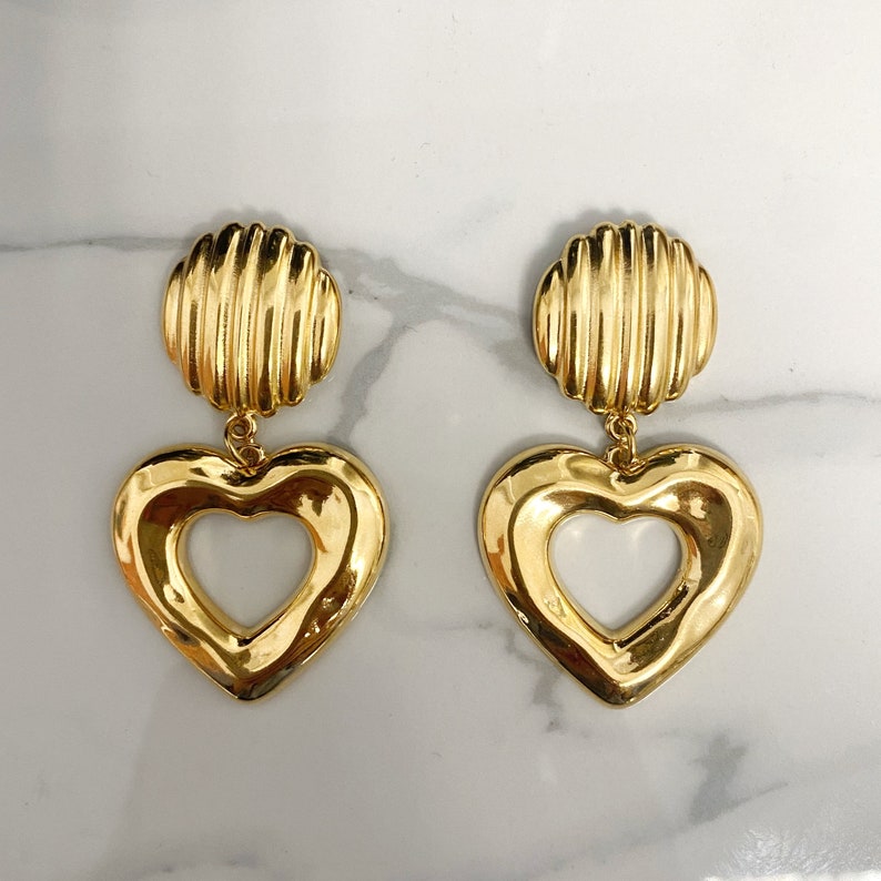 May include: Gold tone heart shaped earrings with a textured round top.