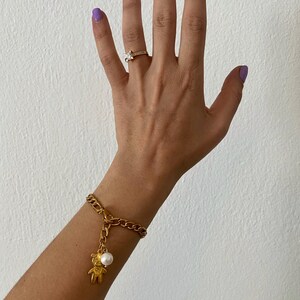 May include: A gold chain bracelet with a small gold bear charm and a white pearl. The bracelet is on a person's wrist.