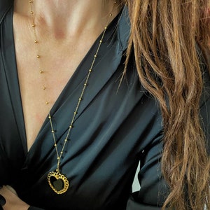 Pu&ograve; includere: Una collana a catena dorata con un ciondolo a forma di cuore nero. Il ciondolo ha un bordo dorato ed &egrave; su uno sfondo nero.