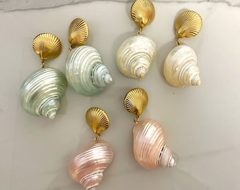 Könnte beinhalten: Sechs Paar goldfarbene Ohrringe mit muschelförmigen Anhängern. Die Anhänger sind in Weiß-, Rosa- und Grüntönen gehalten.