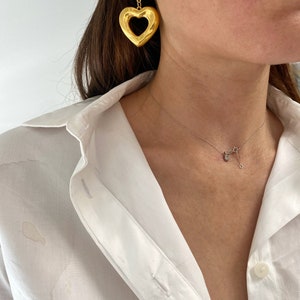 May include: Gold heart-shaped earrings with a textured design. The earrings are dangling and have a smaller, round, textured piece above the heart.