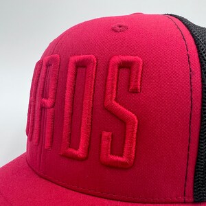K&ouml;nnte beinhalten: Eine rote und schwarze Trucker-Kappe mit dem Wort "BOSS" in rot auf der Vorderseite gestickt.