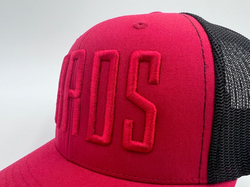 K&ouml;nnte beinhalten: Eine rote und schwarze Trucker-Kappe mit dem Wort "BOSS" in rot auf der Vorderseite gestickt.