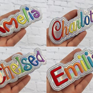 May include: Four rainbow embroidered iron-on patches with the names Amelia, Charlotte, Chelsea, and Emilia. The patches are on a silver iridescent background.