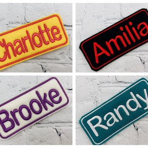 May include: Four embroidered name patches. The top left patch is yellow with the name "Charlotte" in red. The top right patch is black with "Amilia" in red. The bottom left patch is white with "Brooke" in purple. The bottom right patch is teal with "Randy" in white.