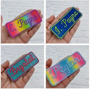May include: Four rectangular embroidered name patches in various colors. Each patch features a name in a cursive font. The patches are held in a hand. The names are: E. Payne, J. Payne, Brystal, and Peyton. The patches have a glittery border.