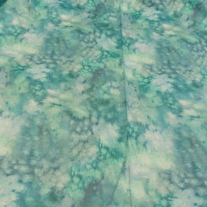 Puede incluir: Primer plano de una tela de teñido anudado de color verde azulado y blanco con un patrón sutil y moteado.