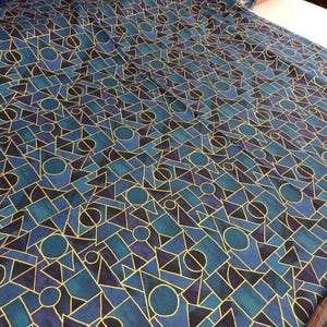 Könnte beinhalten: Blauer und goldener geometrischer Stoff mit einem sich wiederholenden Muster aus Kreisen, Quadraten und Dreiecken.