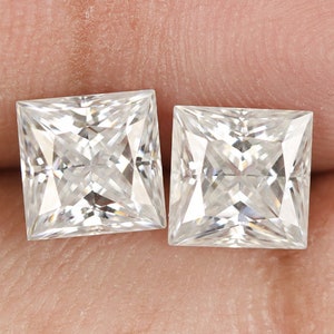 Op de afbeelding: Twee heldere vierkante diamanten, gezet in een kraalbezetting, worden getoond op een vinger.