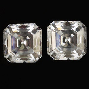 Op de afbeelding: Twee vierkant geslepen, heldere edelstenen met meerdere facetten worden tegen een zwarte achtergrond getoond. De edelstenen zijn naast elkaar geplaatst en tonen hun symmetrische vorm en briljante glans. De stenen lijken diamanten te zijn.