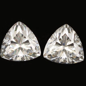 Op de afbeelding: Twee heldere driehoekige edelstenen met een facetgeslepen vorm, tegen een zwarte achtergrond.