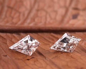 Puede incluir: Dos diamantes en forma de cometa, con múltiples facetas, brillan sobre una superficie de madera marrón texturizada. Las piedras preciosas reflejan la luz, resaltando su brillo. Los diamantes se presentan sobre un fondo natural y orgánico.