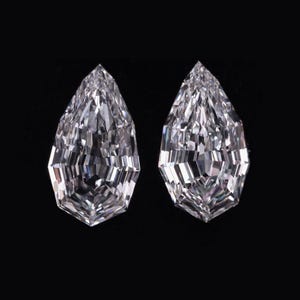 May include: Two loose, clear, colourless gemstones with a shield-like, elongated pentagonal shape and a brilliant faceted cut. Each stone features a pointed top and a flat base, displaying sharp geometric edges and high light reflection.