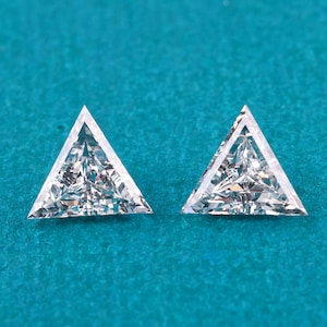 Può includere: Due diamanti a forma triangolare, taglio brillante. Ogni diamante ha un aspetto chiaro e sfaccettato, che riflette la luce. I diamanti sono su uno sfondo verde acqua, evidenziando la loro brillantezza e chiarezza. Ideale per gioielli.