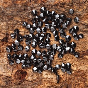May include: A collection of black diamond gemstones scattered on a piece of rough wood.