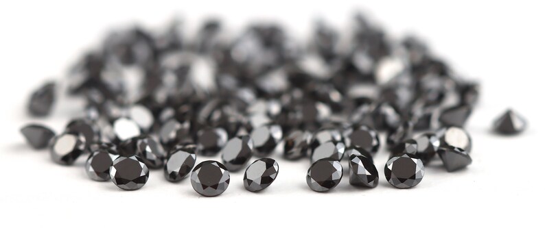 May include: A pile of black diamonds, also known as carbonado diamonds, on a white background.