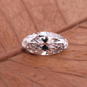 May include: A clear marquise-cut diamond, displaying multiple facets that catch the light. The gemstone sits on a brown, textured surface. The elongated shape of the diamond is a key feature, highlighting its sparkle. The image showcases a piece of jewelry, a gemstone.