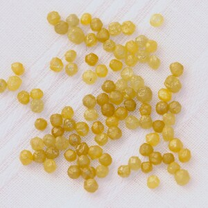 May include: A collection of small, yellow, faceted gemstones, likely diamonds, scattered on a white fabric surface.