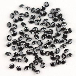 May include: A scattering of black round gemstones, likely diamonds, on a white surface. The stones are various sizes and have a faceted cut.