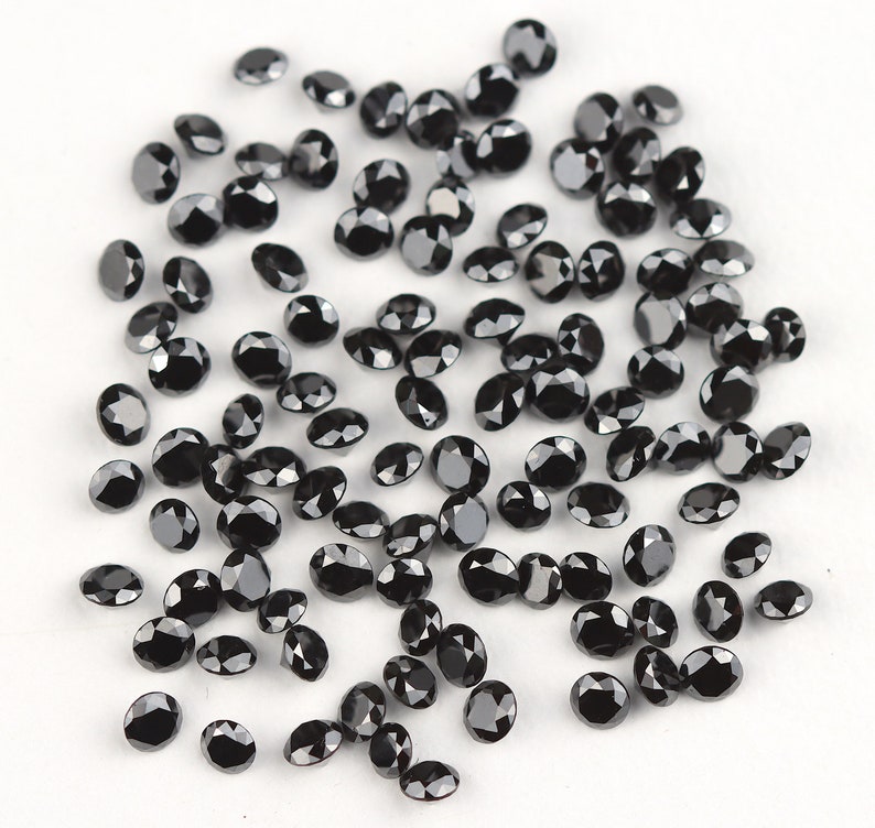 May include: A scattering of black round gemstones, likely diamonds, on a white surface. The stones are various sizes and have a faceted cut.