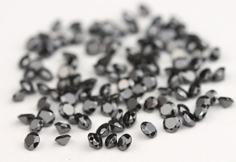 May include: A scattering of black diamonds on a white surface. The diamonds are round and have a brilliant cut.
