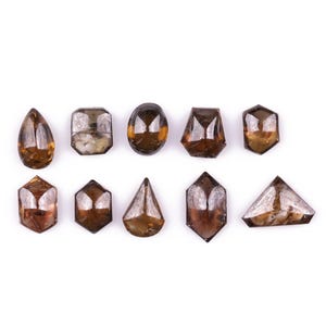 May include: Ten uncut gemstones in various shapes, including teardrop, oval, and geometric forms. The stones are amber-brown and translucent, displayed against a white background. Each stone is unique in shape and size.
