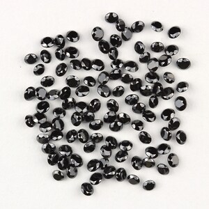 May include: A collection of black oval-shaped gemstones. The gemstones are scattered on a white surface.