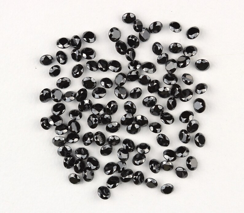 May include: A collection of black oval-shaped gemstones. The gemstones are scattered on a white surface.