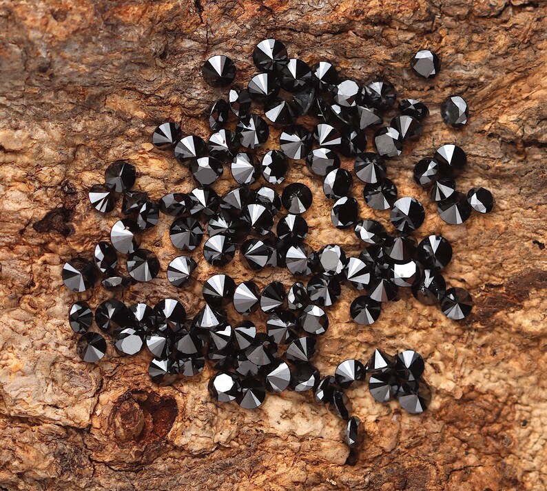 May include: A collection of black diamond gemstones scattered on a piece of rough wood.