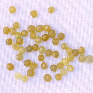 May include: A collection of small, yellow, faceted diamonds scattered on a white fabric background.
