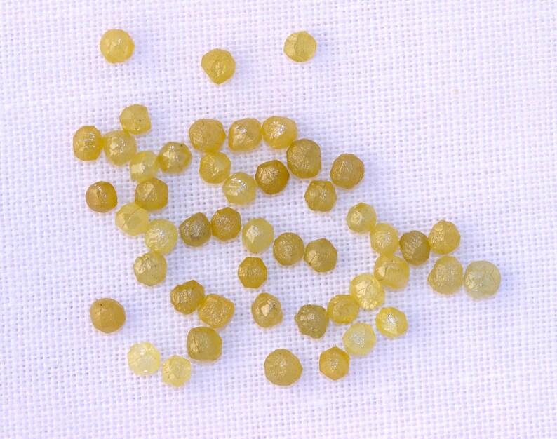 May include: A collection of small, yellow, faceted diamonds scattered on a white fabric background.