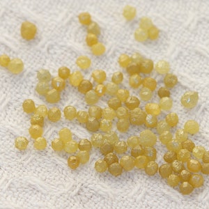 May include: A collection of small, yellow, faceted diamonds on a white knitted surface.