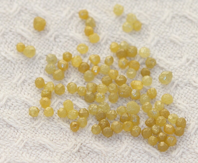 May include: A collection of small, yellow, faceted diamonds on a white knitted surface.