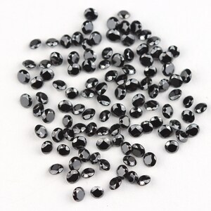 May include: A scattering of black round gemstones on a white surface. The gemstones are various sizes and have a shiny, polished finish.