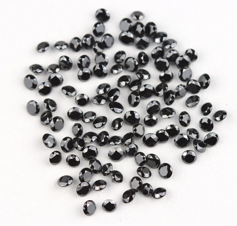 May include: A scattering of black round gemstones on a white surface. The gemstones are various sizes and have a shiny, polished finish.
