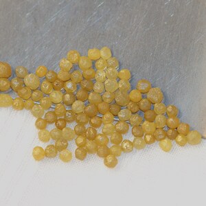 May include: A collection of small, yellow, faceted diamonds. The diamonds are scattered on a white surface.