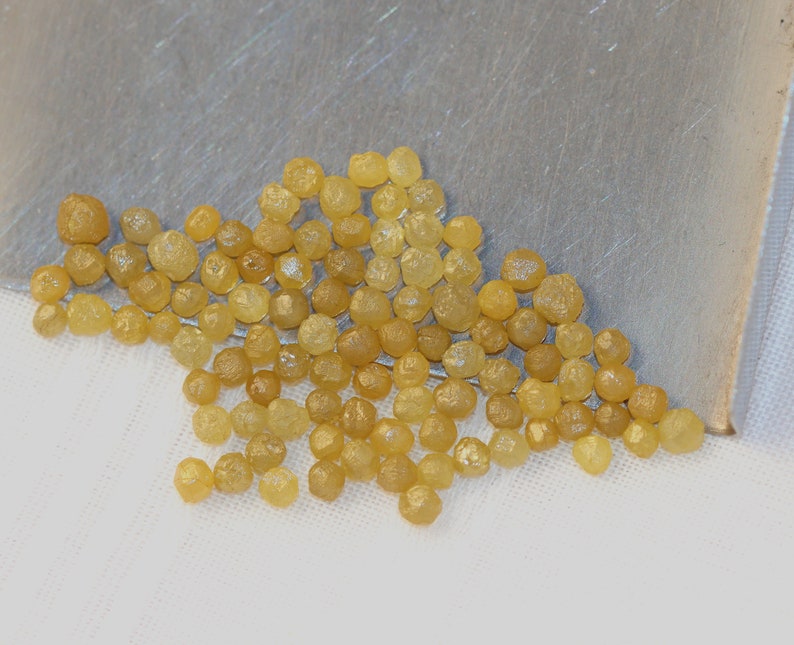 May include: A collection of small, yellow, faceted diamonds. The diamonds are scattered on a white surface.