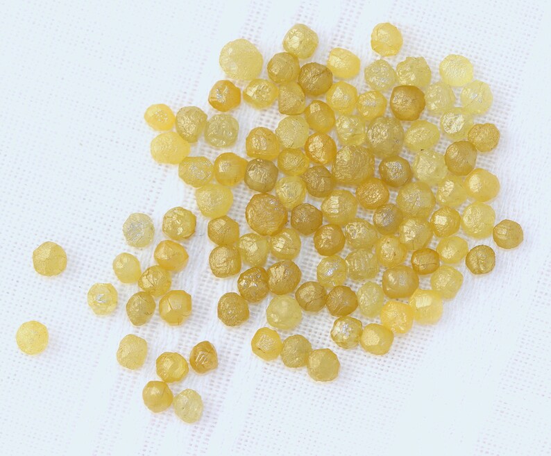 May include: A pile of small, yellow, faceted diamonds on a white surface.