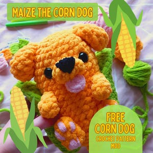 Puede incluir: Un juguete de peluche de perro de maíz tejido a crochet en naranja y rosa, con una mazorca de maíz verde. El juguete está sentado sobre una superficie de crochet verde y blanca. El texto "MAIZE THE CORN DOG" está en la parte superior de la imagen. El texto "FREE CORN DOG CROCHET PATTERN MOD" está en la parte inferior de la imagen.